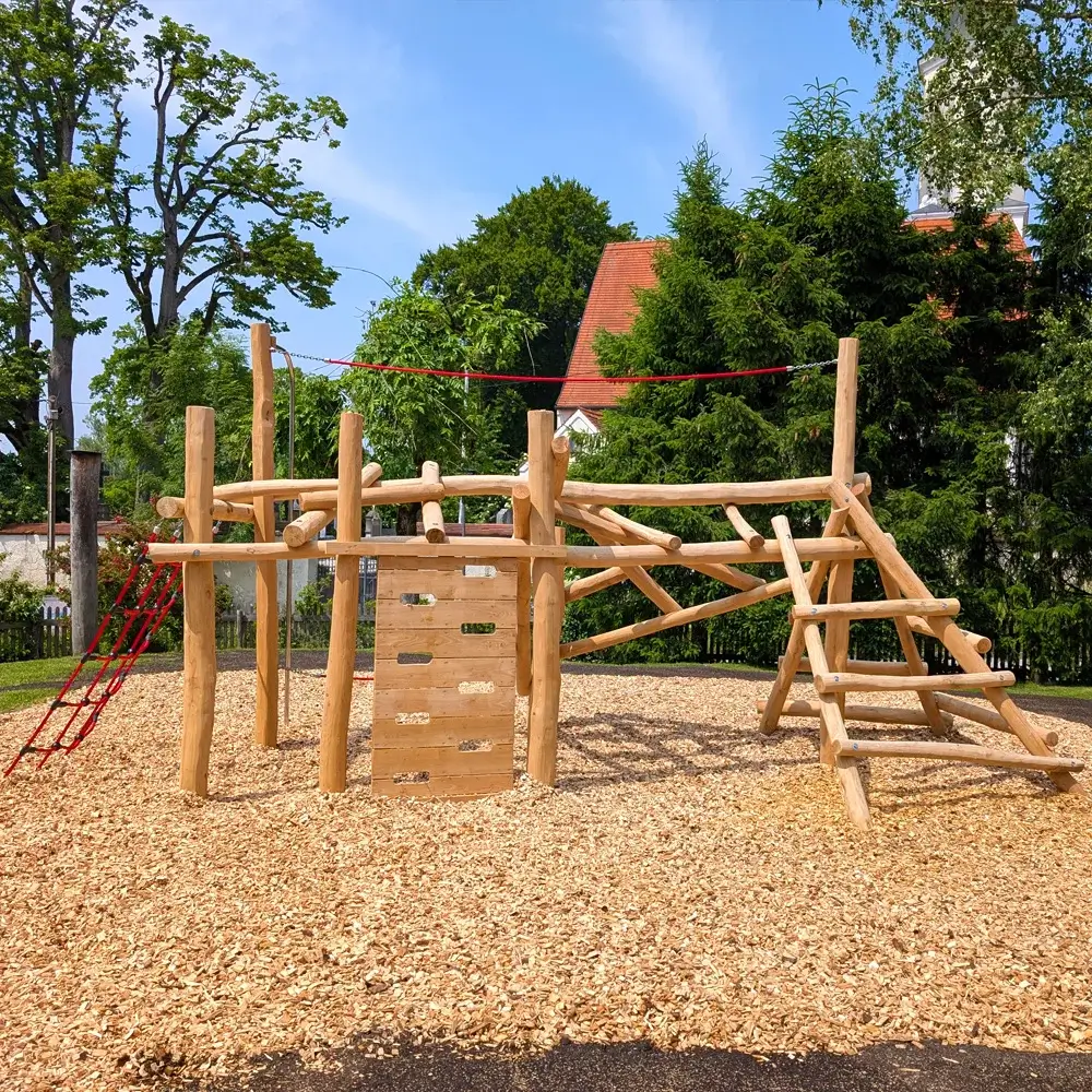 Klettergerüst Faultier aus natürlichen Robinienstämmen mit Kletternetz, Kletterwand mit Tritt- und Grifflöchern und einigen Halteseilen. Platziert auf Fallschutz aus Hackschnitzeln