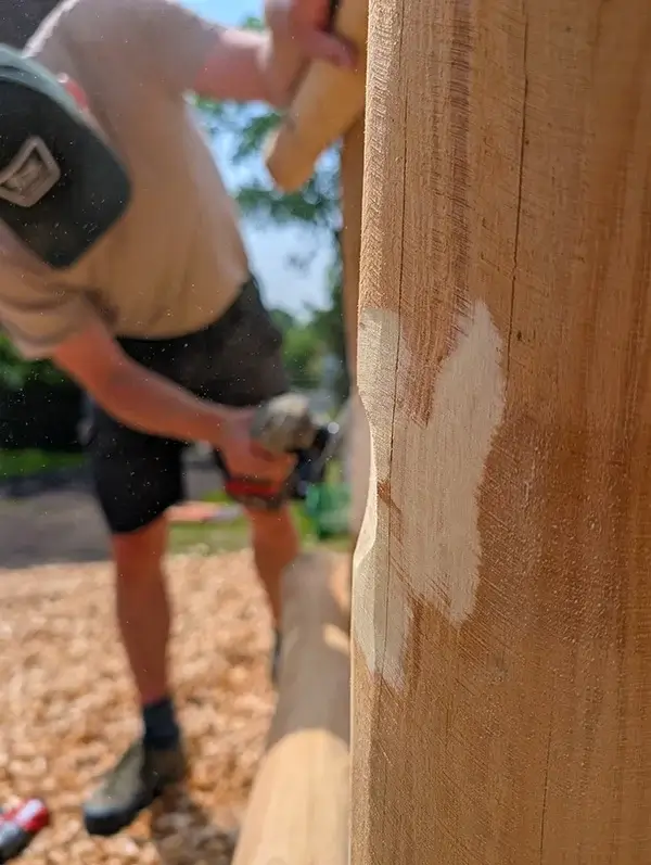 Reparatur eines Spielgeräts. Detailaufnahme einer abgeschliffenen Stelle an einem Robinienpfosten. Im Hintergrund Handwerke mit Winkelschleifer