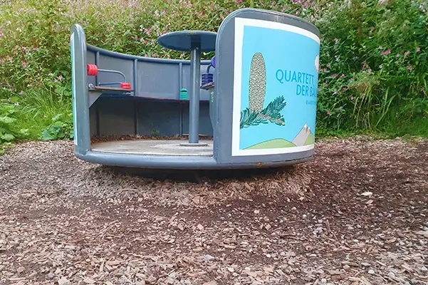 Bodennahe Seitenansicht eines Karussells auf Fallschutz aus Hackschnitzeln. Besonders im rechten Bildteil sieht man den Wegspieleffekt sehr gut. Hier ist eine stark ausgebildete Mulde im Boden um das Karussell zu erkennen.